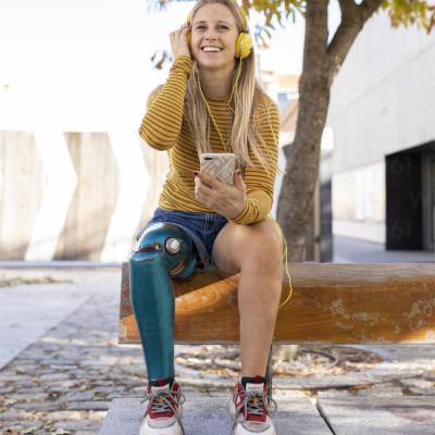 Front View Of Smiling Female With Bionic Leg Prosthesis Sitting In Street And Enjoying Music In Headphones On Sunny Day Adsf20072